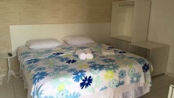 Un lit bien fait, recouvert d’une couvre-lit à motifs floraux, une table de chevet avec une télécommande et une armoire dans une chambre d’hôtel.