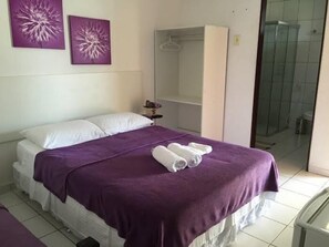 A bedroom with a bed, purple bedding, two wall-mounted flower paintings, a walk-in closet, and a shower area. - Villa Joia Pousada (Barra de São Miguel)