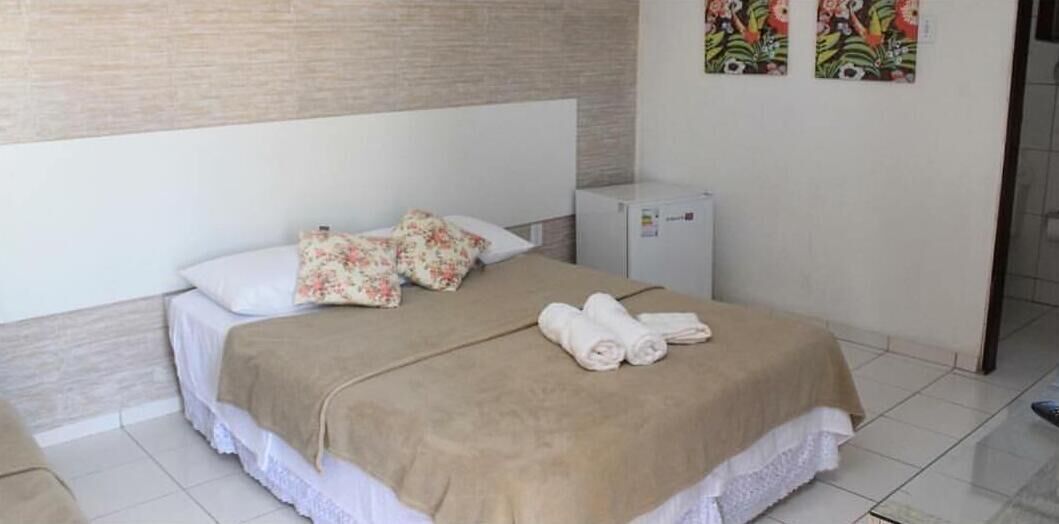 A hotel room with a bed, a small refrigerator, and a wall with floral artwork.