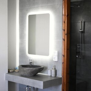 Un baño con un espejo grande, un lavamanos sobre encimera y una ducha.