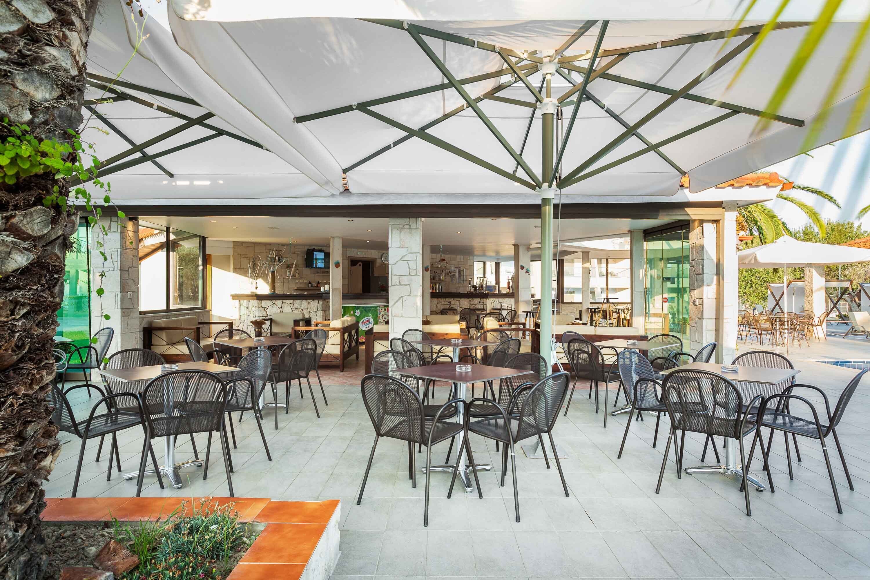 Un espace de restauration en plein air, doté de nombreuses tables et chaises, protégé par de grands parasols, et offrant une vue sur l’espace de restauration intérieur.