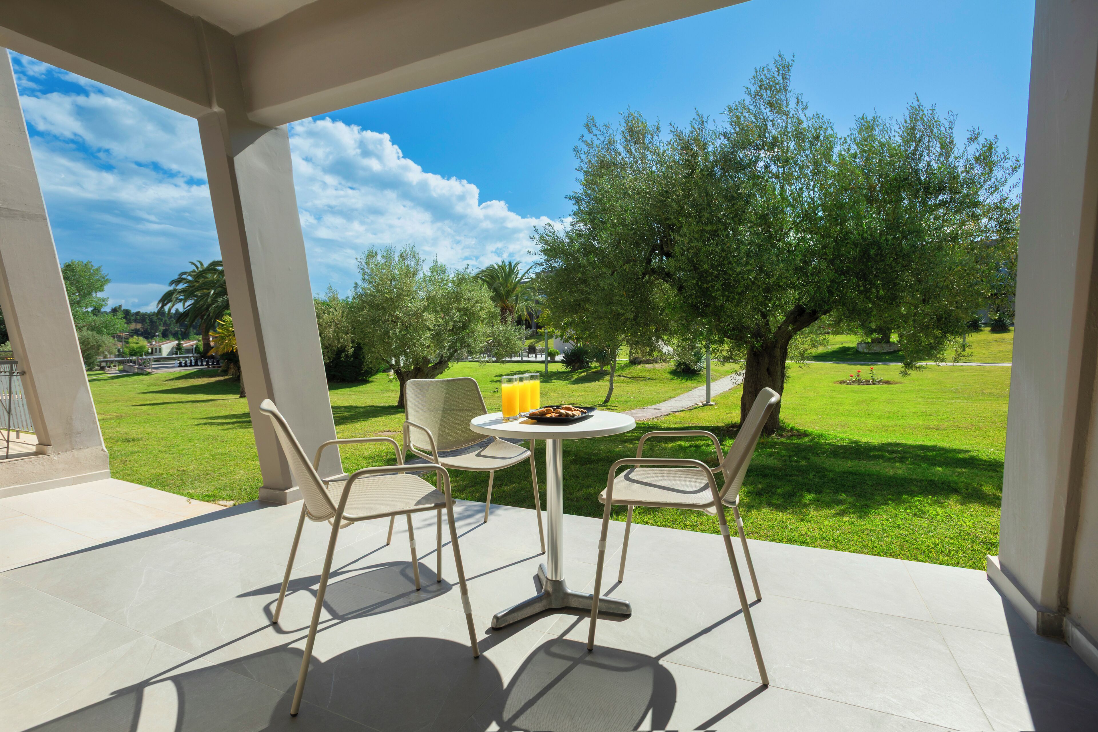 An outdoor patio with a table and chairs, overlooking a well-maintained lawn and trees.