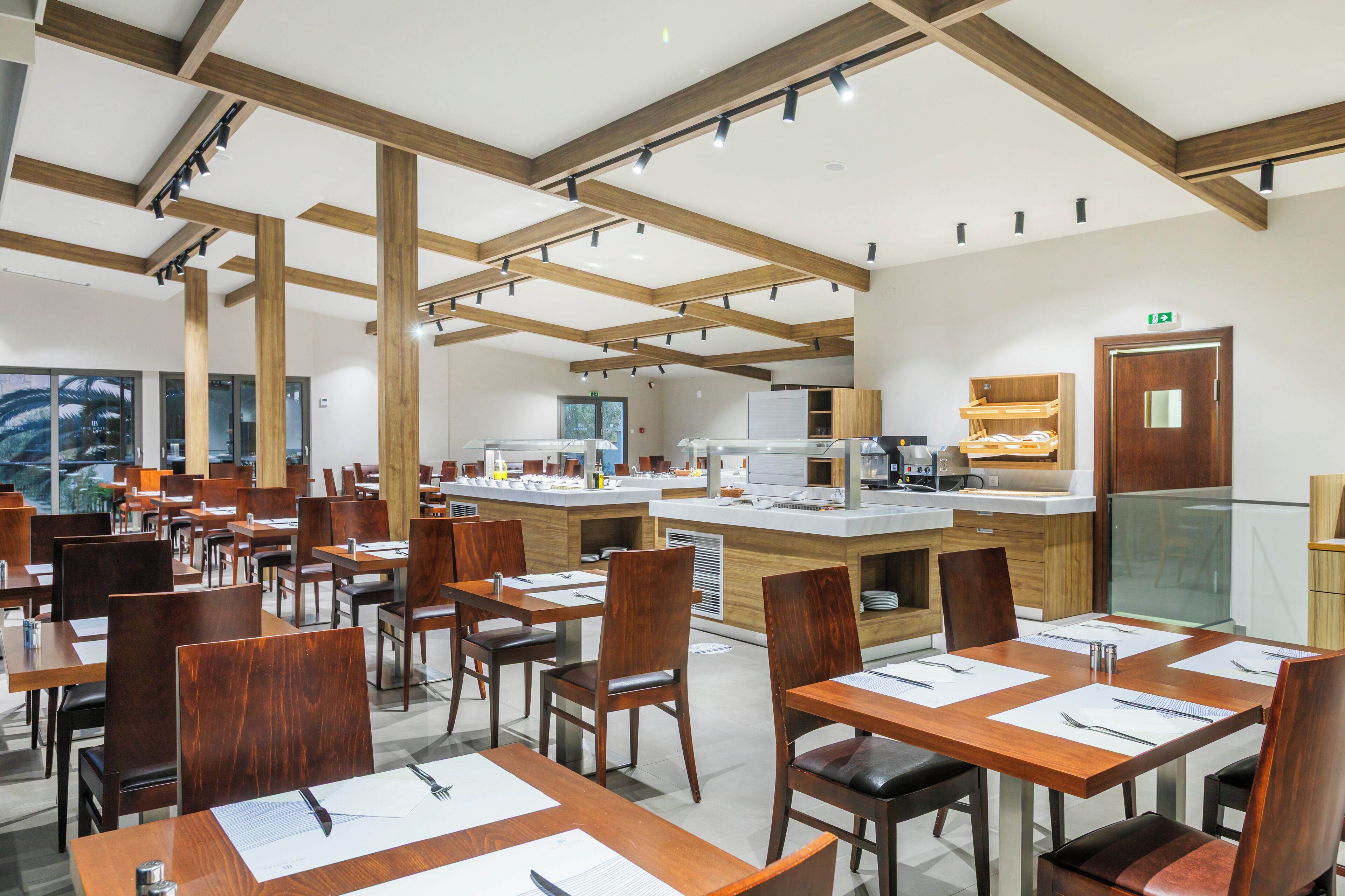 A modern restaurant with wooden beams, multiple dining tables, and a central kitchen area.