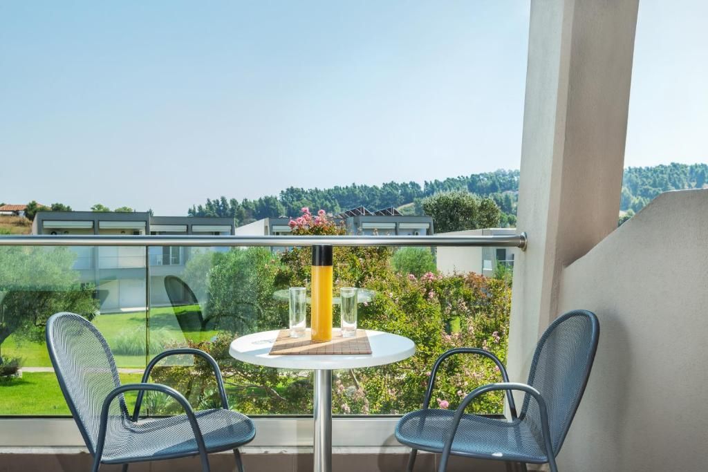 A balcony with a table and chairs, overlooking a garden and buildings.
