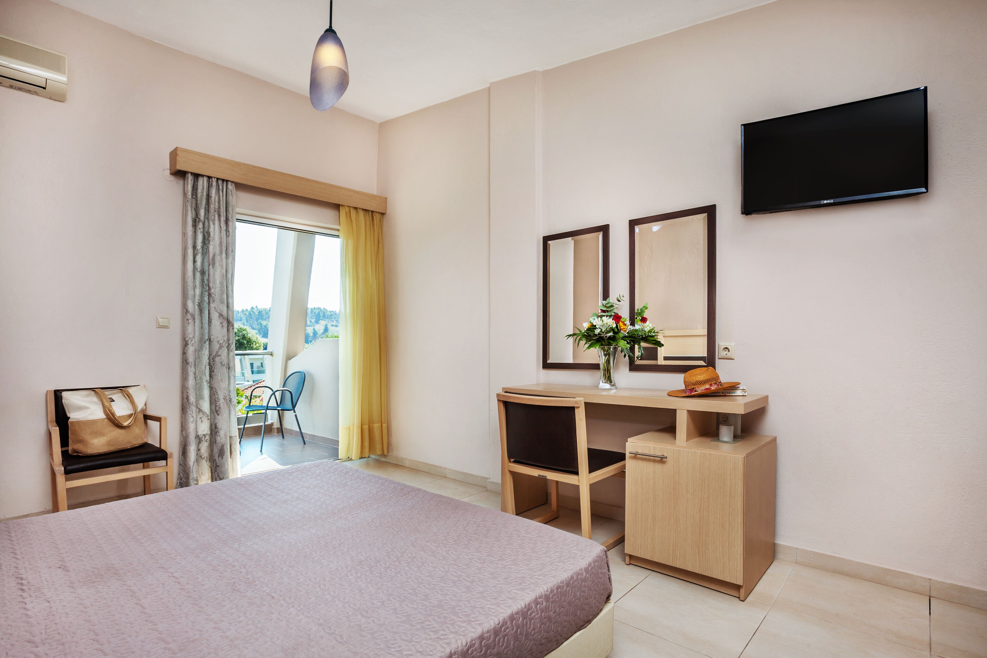 A hotel room with a bed, a desk, a chair, a TV, and a window with curtains.