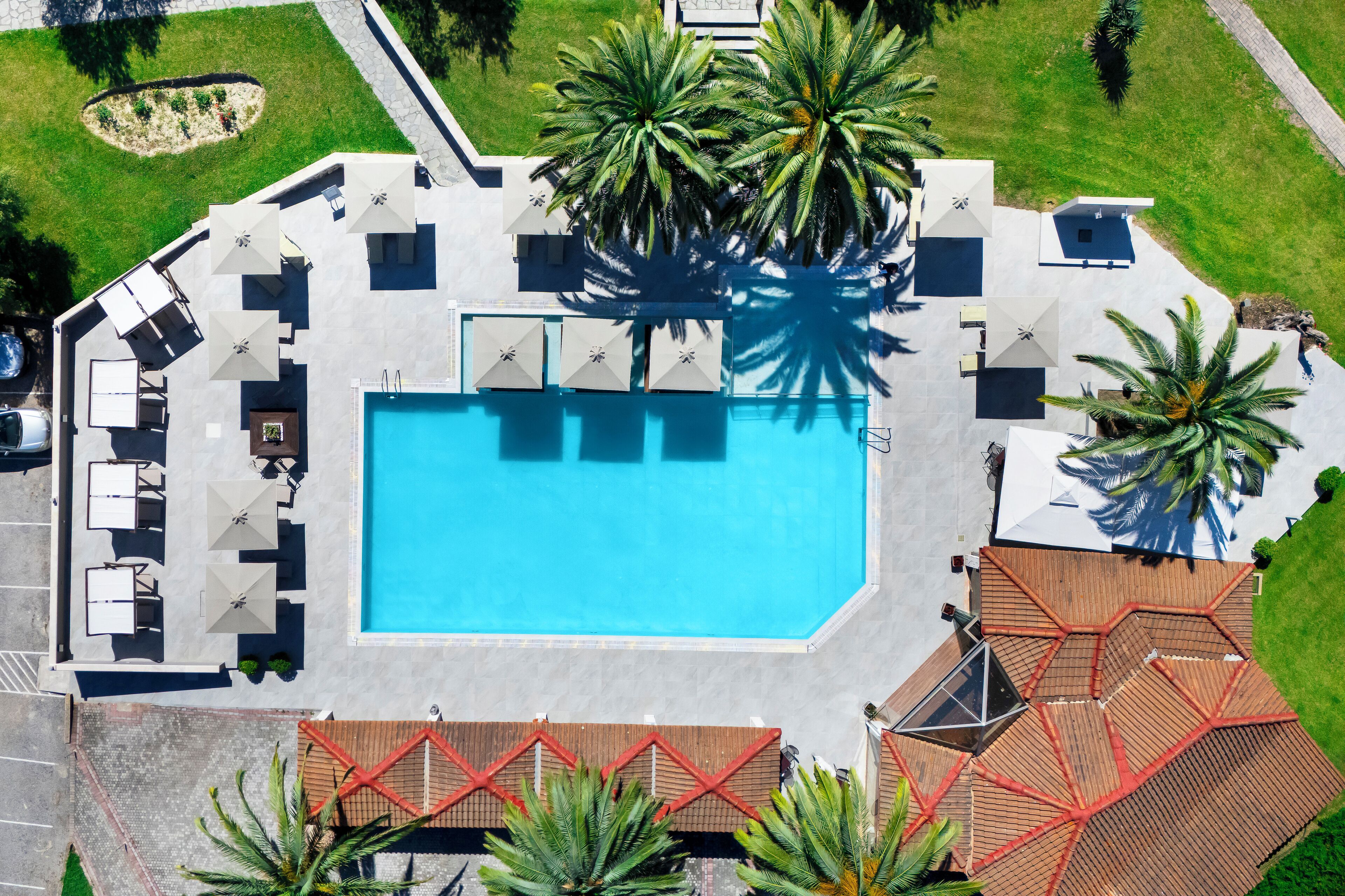 An aerial view of a resort with a swimming pool, sun loungers, and palm trees.
