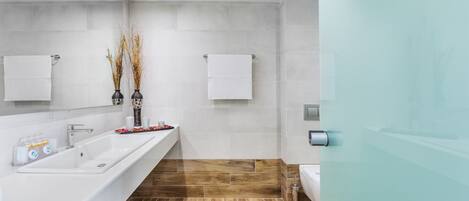 A modern bathroom with a long white sink, two white towels, and a glass shower enclosure.