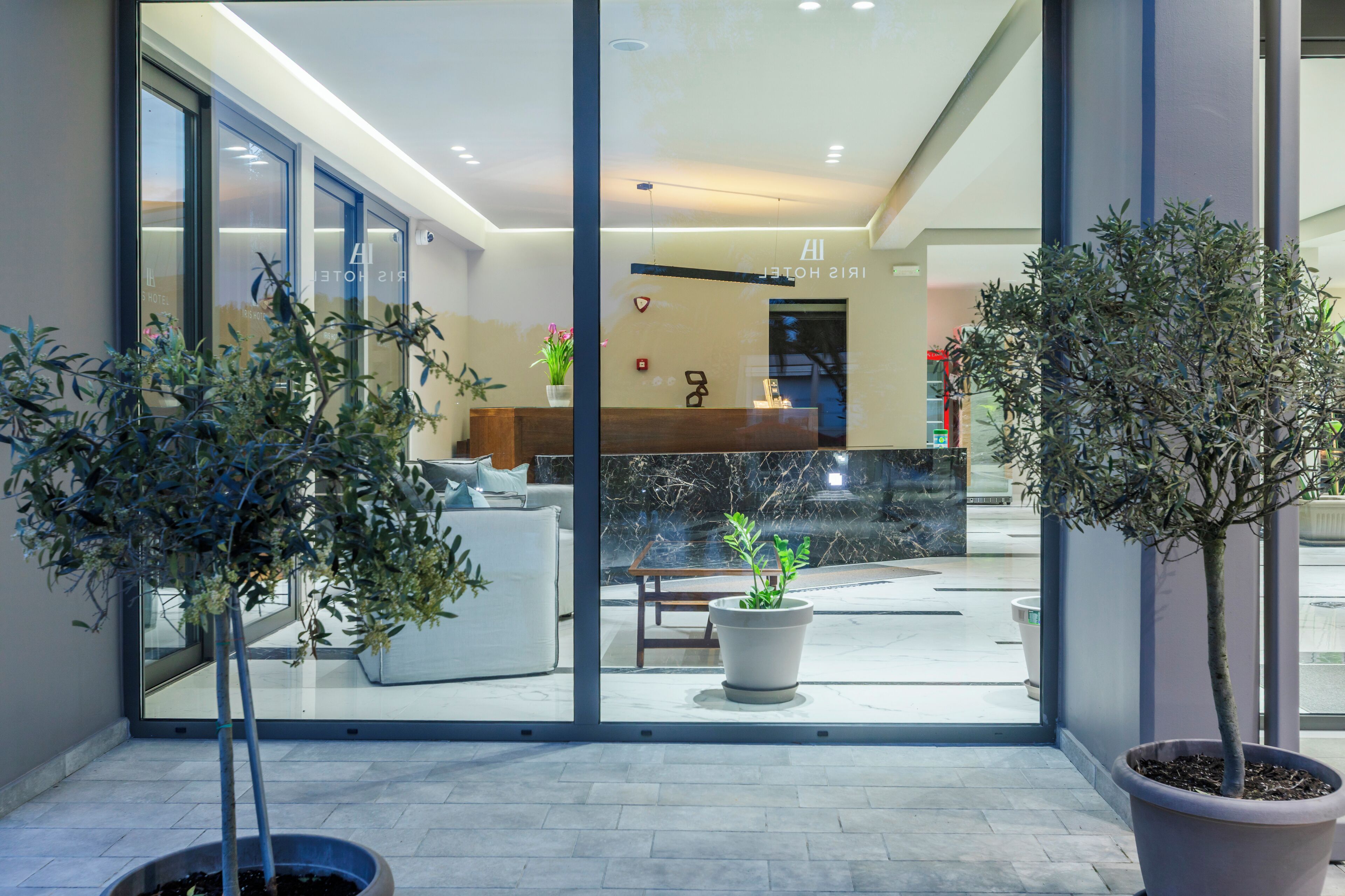 Un moderno vestíbulo de hotel con mostrador de recepción, puertas de vidrio y plantas en macetas.