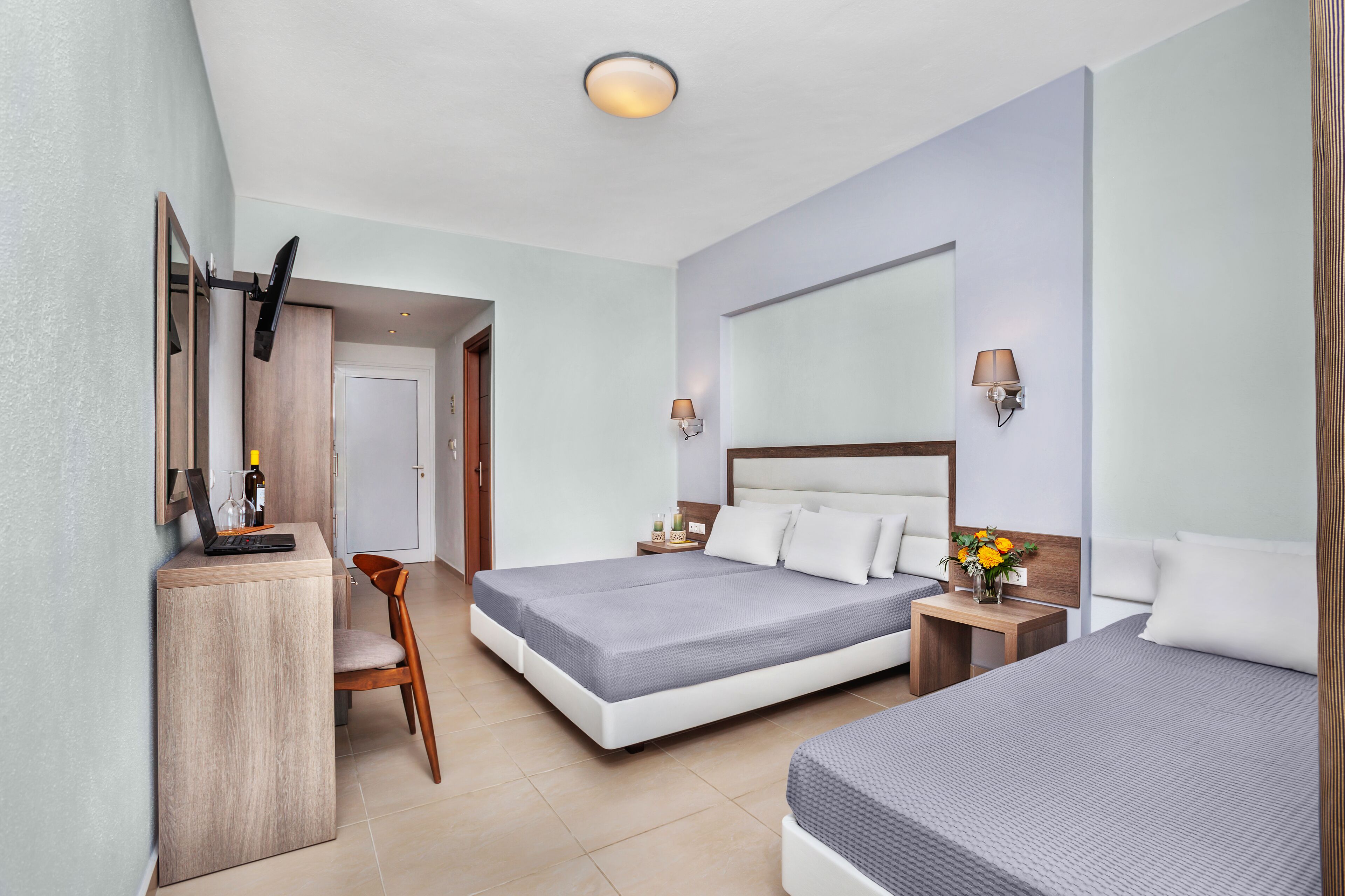A hotel room with a bed, bedside table, lamp, and a desk with a chair.