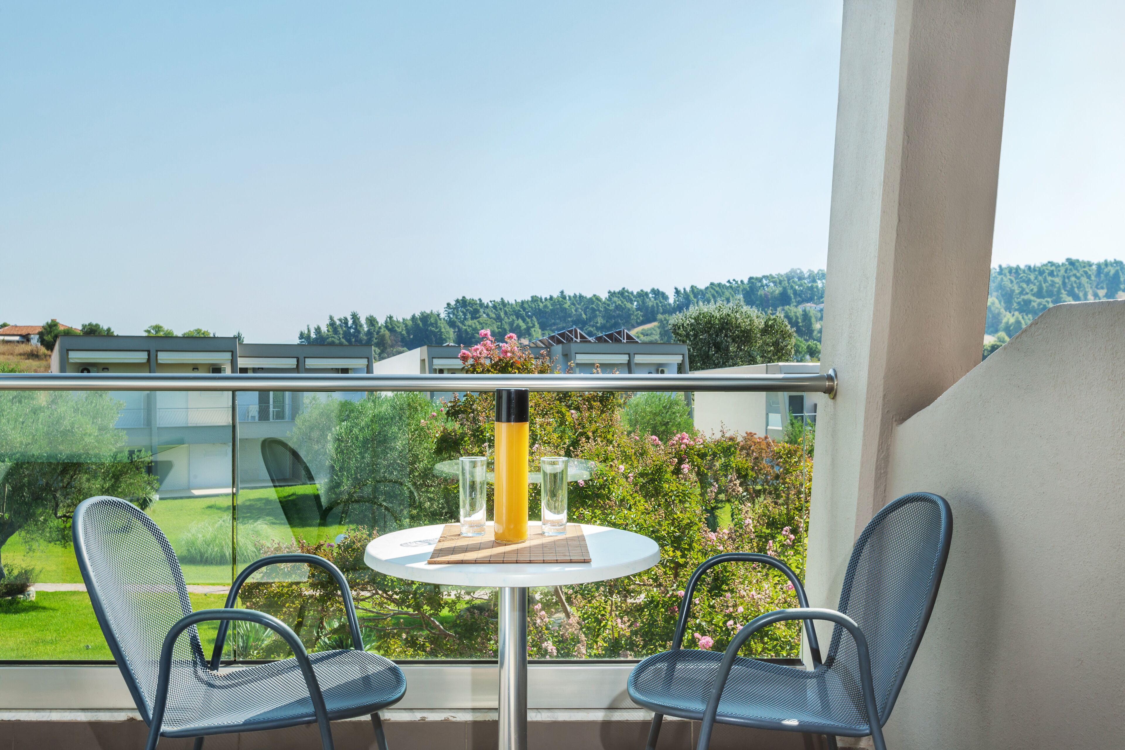 Un balcón con dos sillas y una mesa, con vistas a un jardín y edificios.