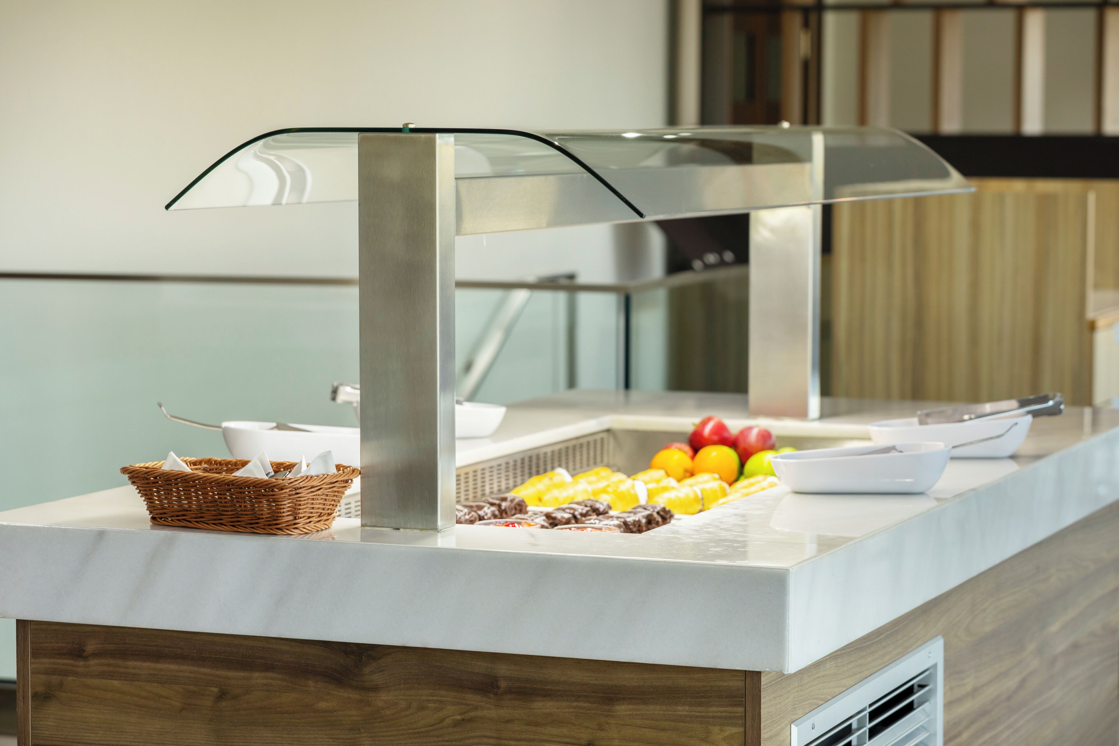 A buffet setup with a glass-covered food display, a wicker basket, and various fruits and vegetables.