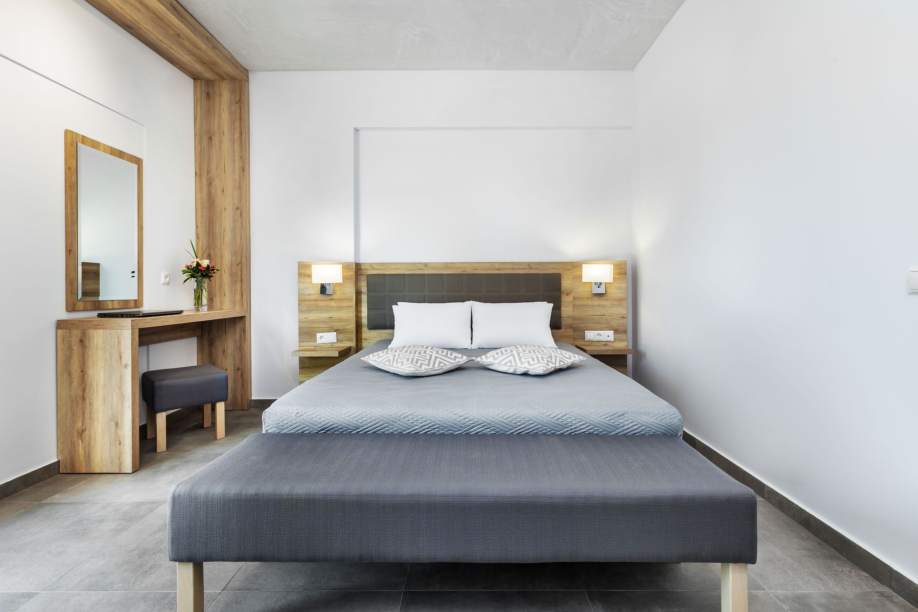 A modern bedroom with a bed, bedside tables, a desk, and a mirror.