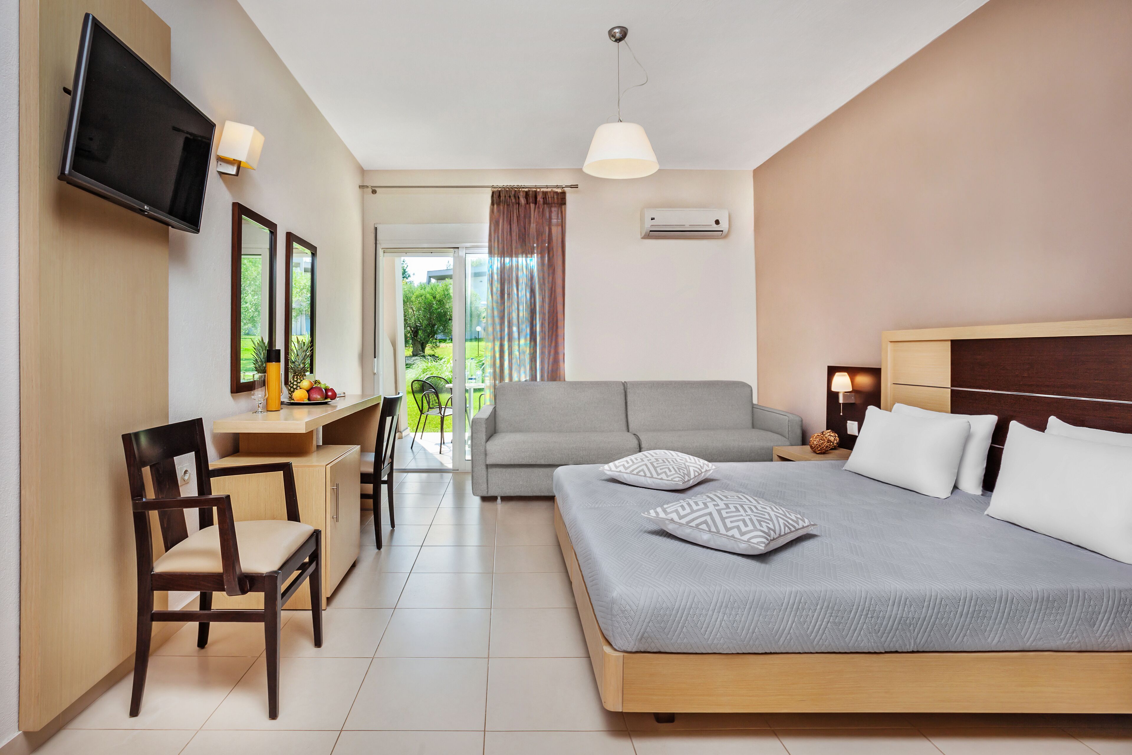A modern hotel room with a bed, a sofa, a desk, and a TV.