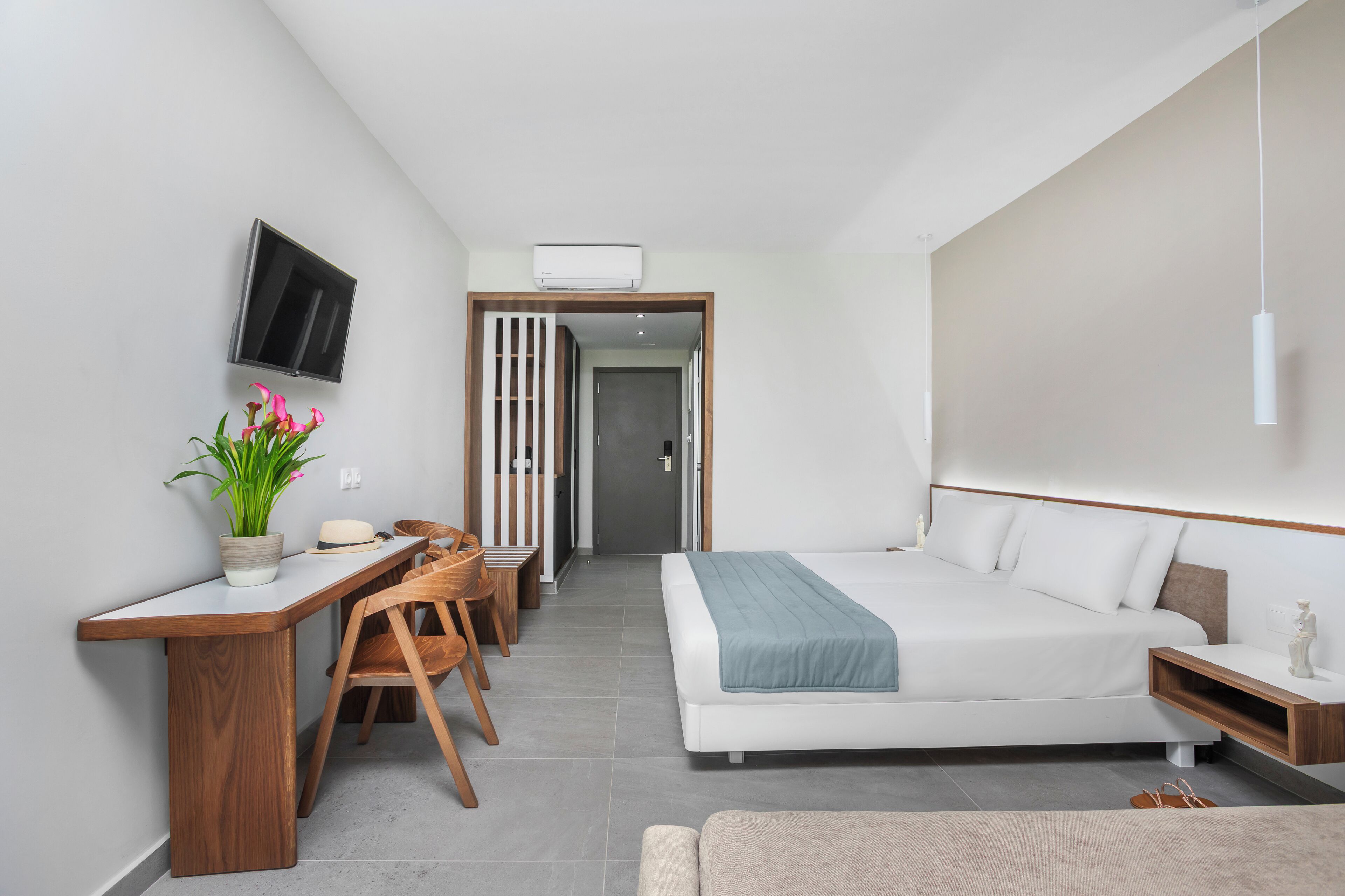A modern bedroom with a bed, bedside table, TV, desk, chair, and a potted plant.