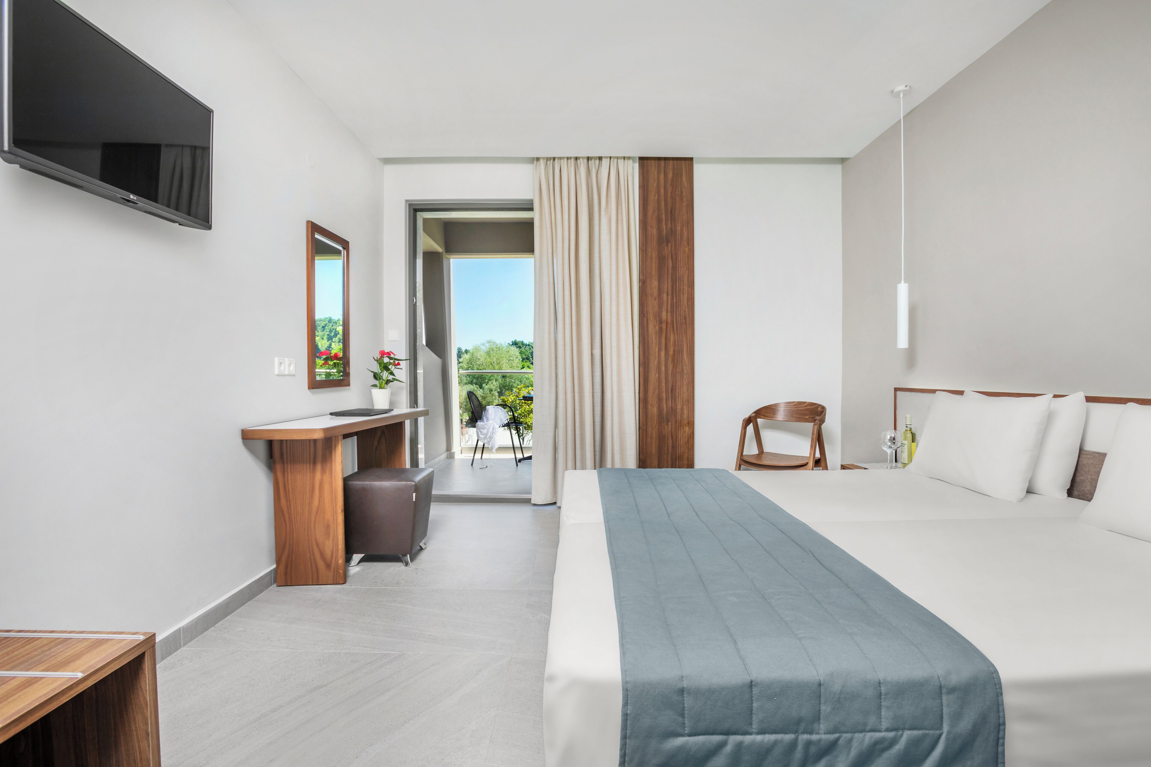 A modern hotel room with a bed, a desk, a chair, a TV, and a balcony with a view.
