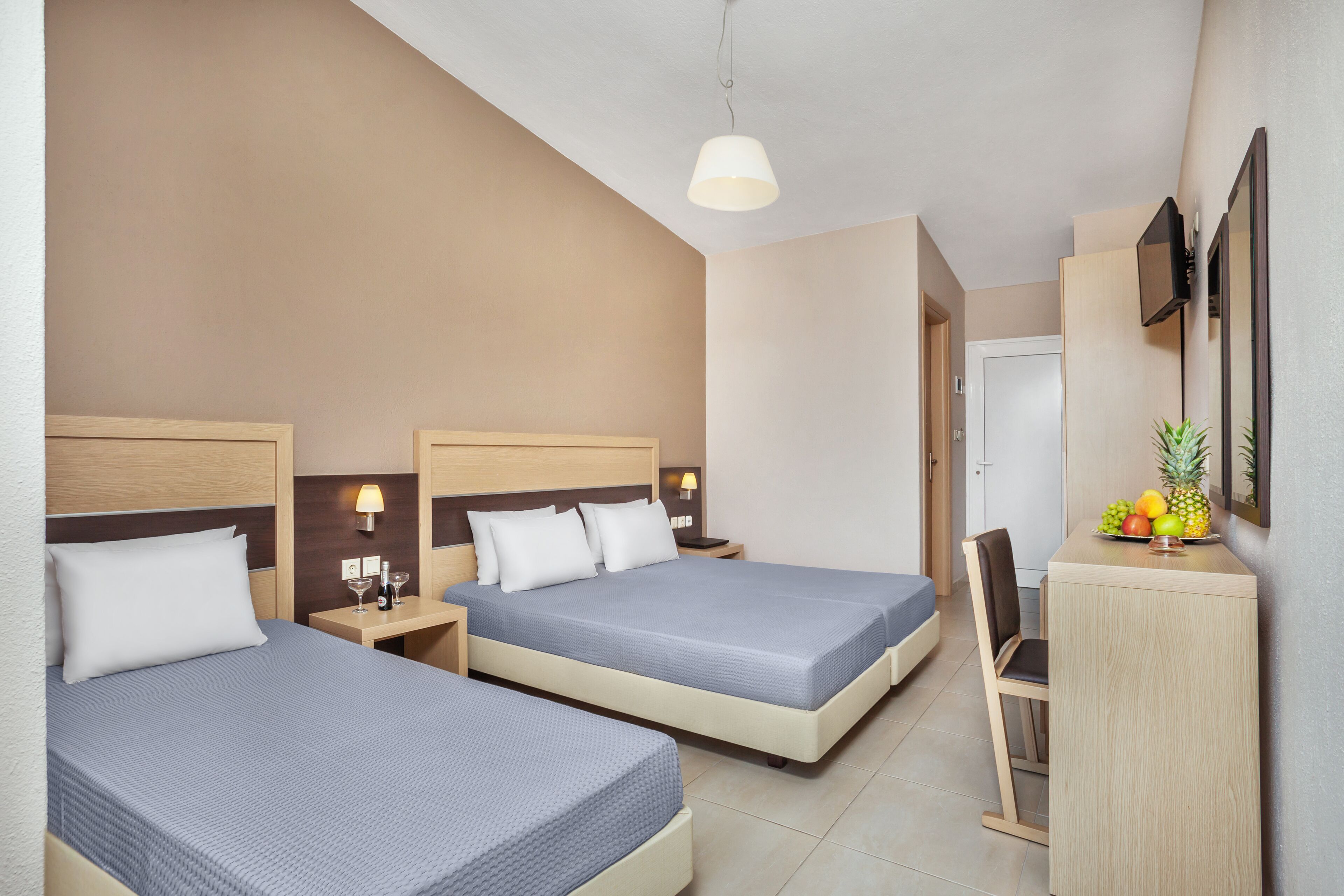 A hotel room with two beds, a desk, a chair, and a small kitchenette area.