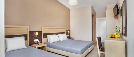 A hotel room with two beds, a desk, a chair, and a small kitchenette area.