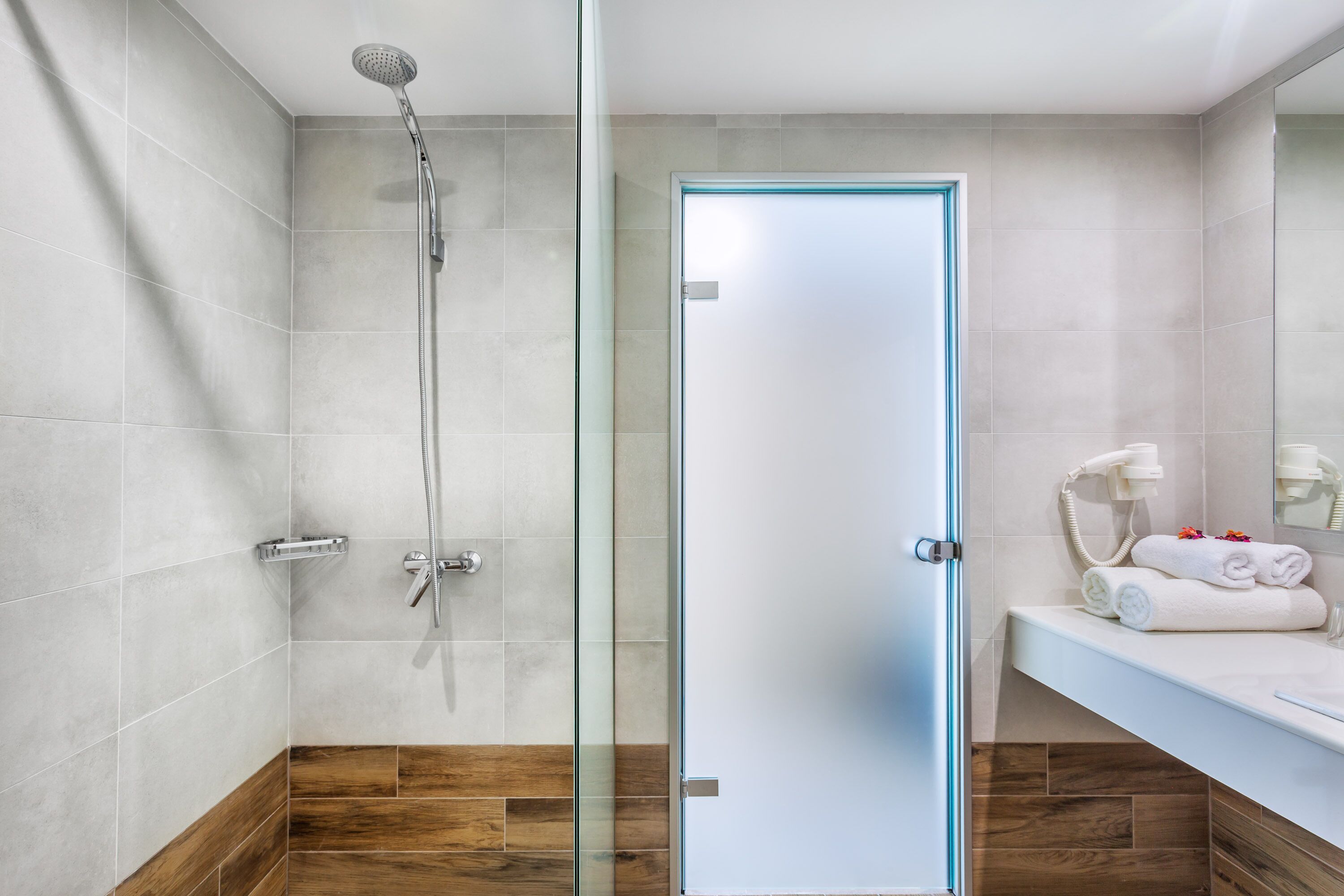 A modern bathroom with a glass shower enclosure, a wooden floor, and a white vanity with towels.