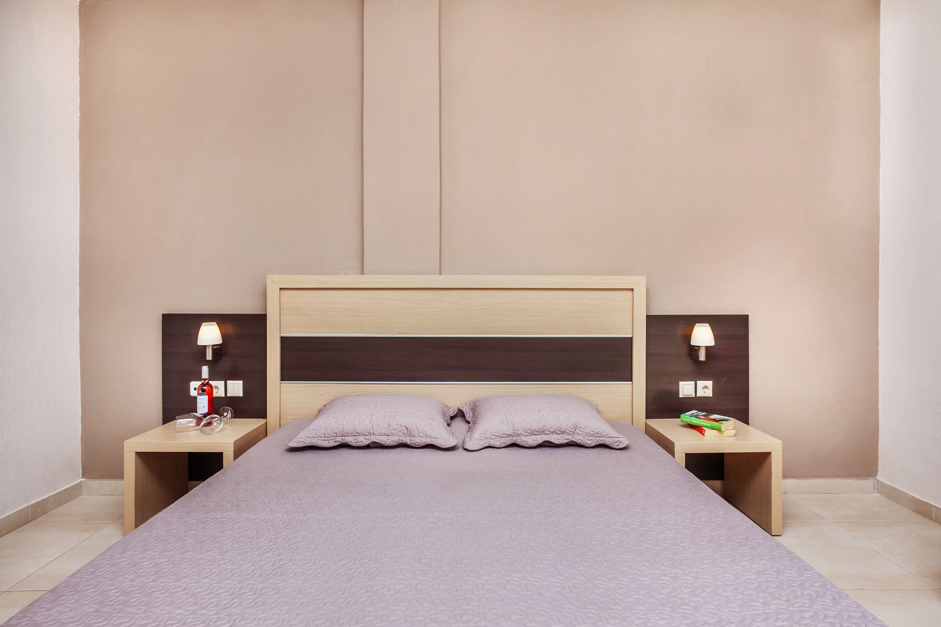 A neatly arranged hotel room with a large bed, two bedside tables, and a headboard.
