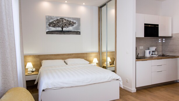 Une chambre d’hôtel moderne avec un lit bien fait, une petite kitchenette et un tableau accroché au mur.