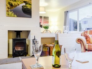 A cozy room with a fireplace, a table with wine glasses and a bottle, and a window with a view of a house. - Coastal Bolthole - Great accommodation on the North Norfolk coast. (Kings Lynn)