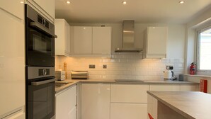 Una cucina moderna con mobili bianchi, forno integrato e cappa aspirante in acciaio inossidabile.
