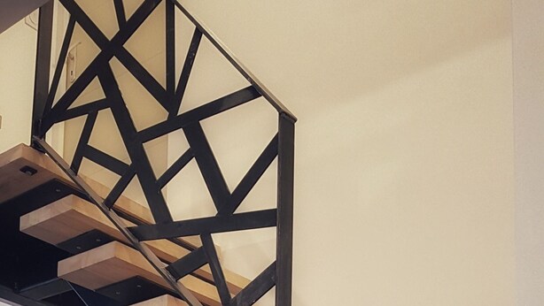 A modern staircase with wooden steps and a geometric metal railing.