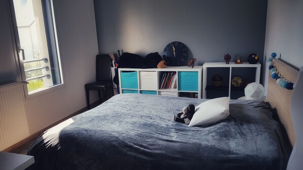 Un dormitorio con cama, ventana, escritorio y estantería.