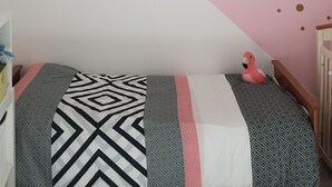 A bedroom with a bed, a pink wall with gold dots, and a white ceiling light fixture.
