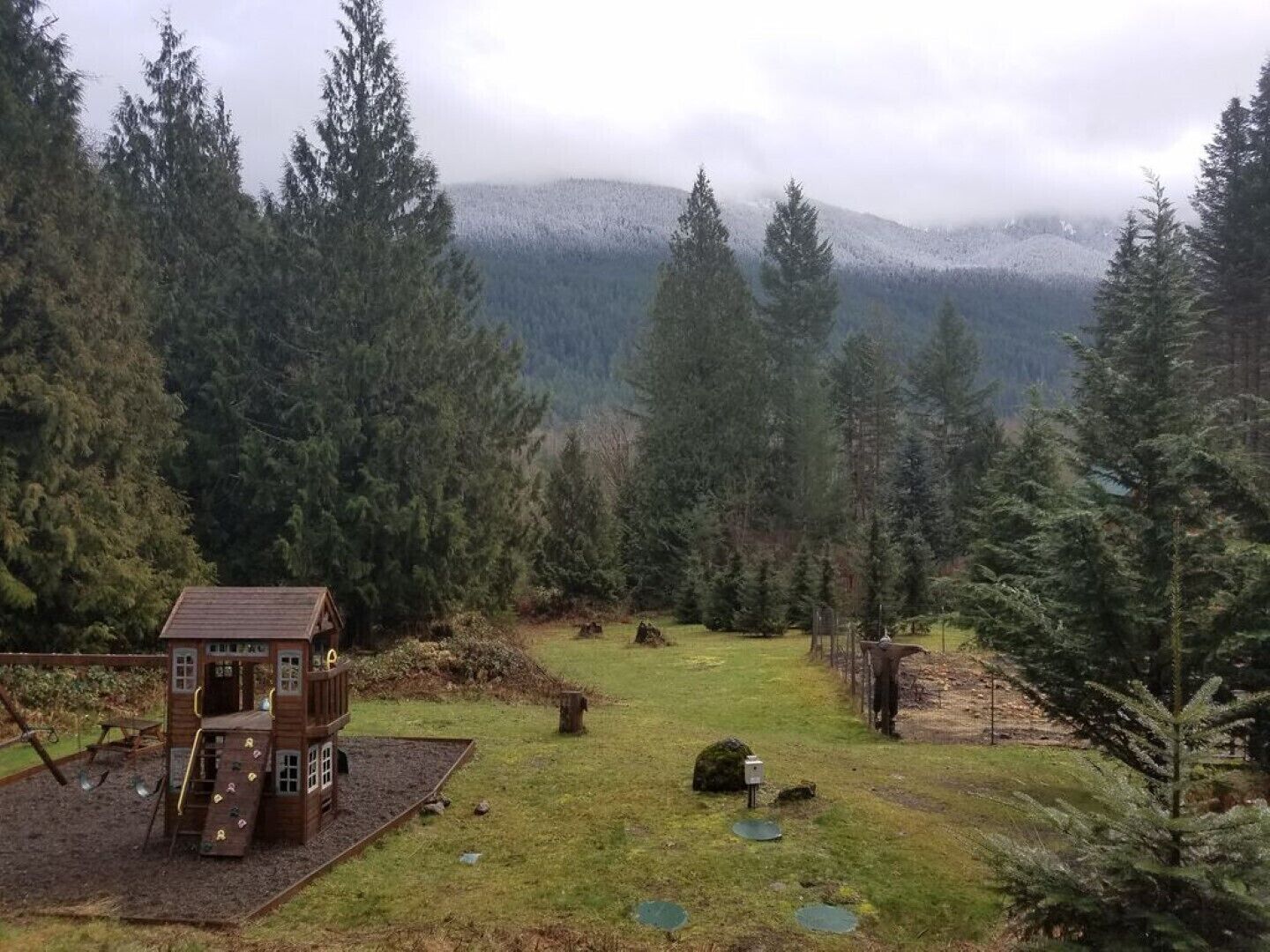 Una cabaña de madera con un porche y un columpio en un área boscosa con vistas a una cadena montañosa.