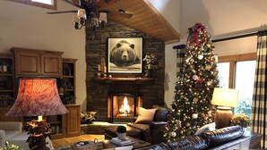 Ein gemütliches Wohnzimmer mit Kamin aus Stein, einem Weihnachtsbaum, Ledermöbeln und einem großen Bärenbild.
