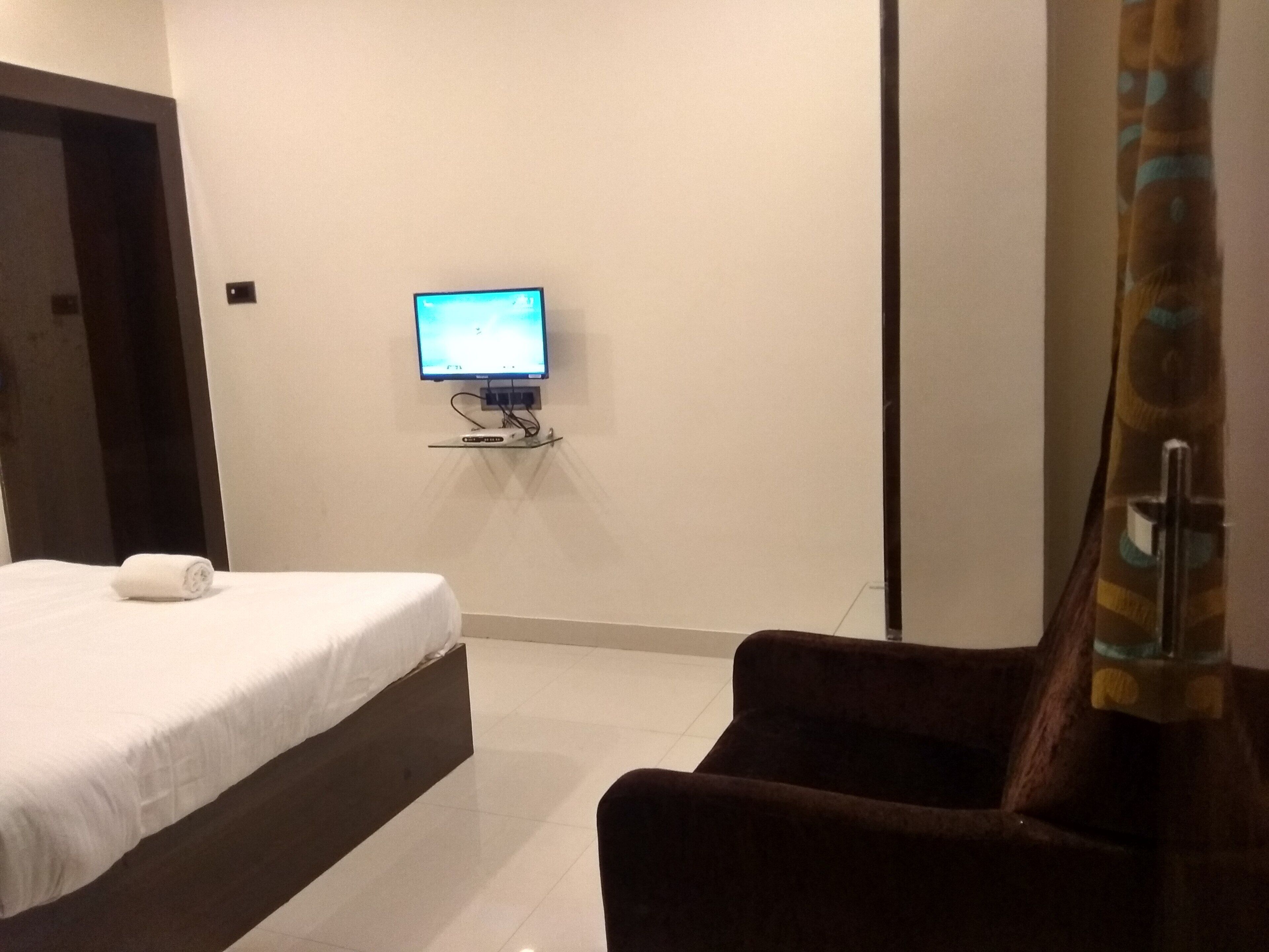 Una habitación de hotel con una cama, un televisor montado en la pared y una silla.