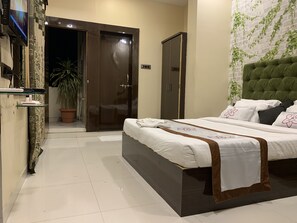 Habitación de hotel con cama, armario, planta en maceta y televisor en la pared.