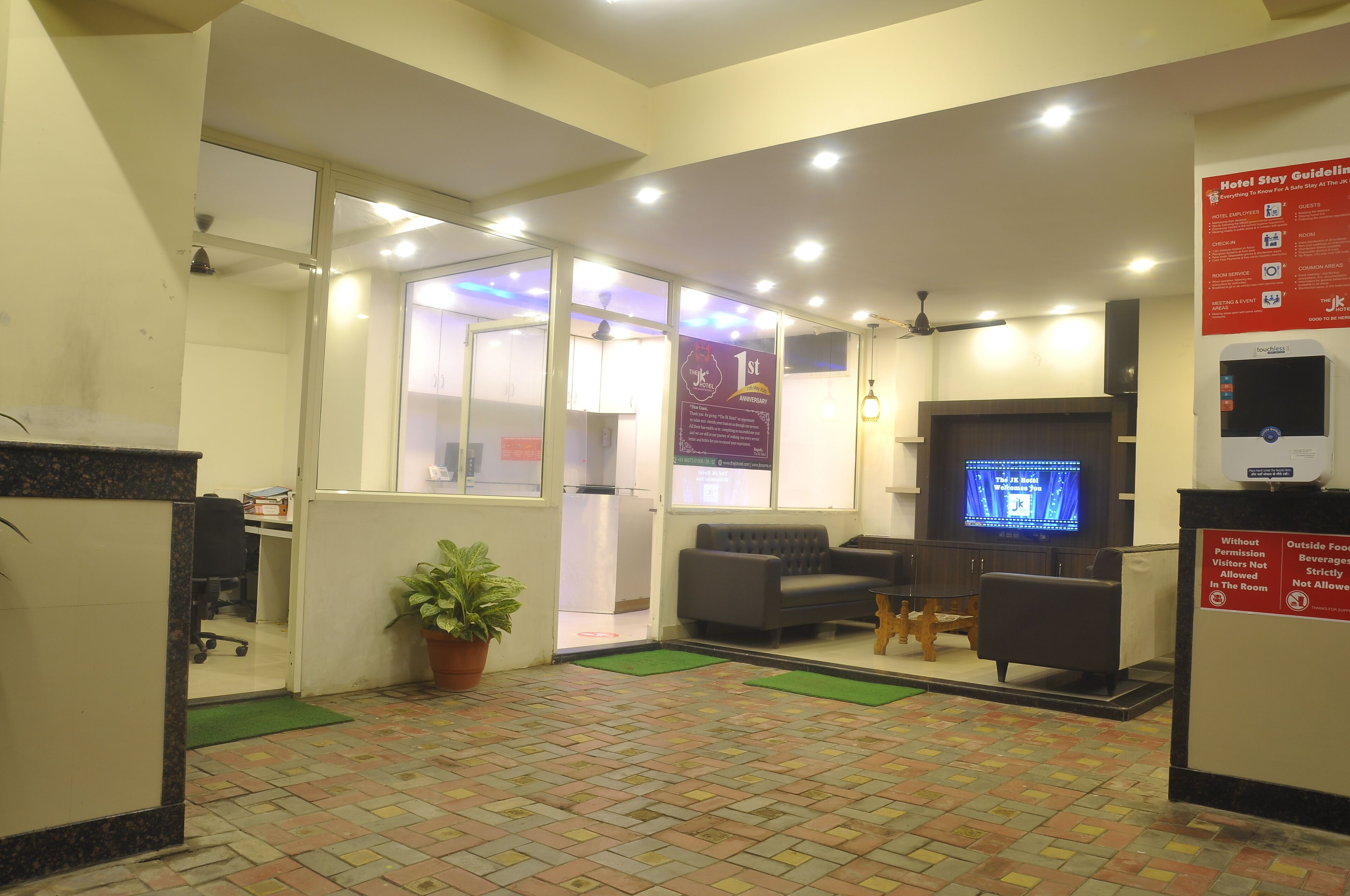 A hotel reception area with a reception desk, seating area, and a television screen.