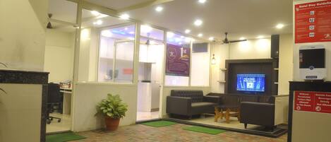 A hotel reception area with a reception desk, seating area, and a television screen.