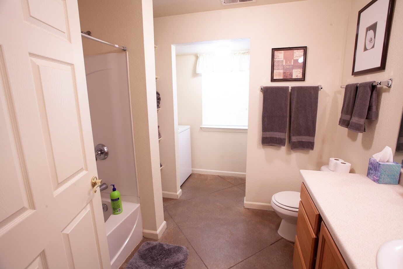 A bathroom with a bathtub, toilet, and sink. There are towels hanging on the wall and a picture frame.