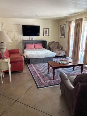 Une chambre à coucher avec un lit, une télévision, un fauteuil rouge, un fauteuil à motifs et une table basse.