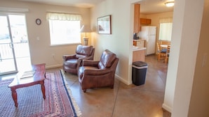 A living room with two leather chairs, a small table, a patterned rug, and a kitchen in the background.