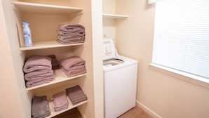A laundry room with a washing machine, shelves with folded towels, and a bottle of detergent.