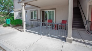 A two-story building with a covered balcony, a staircase, and a small patio area with outdoor furniture.