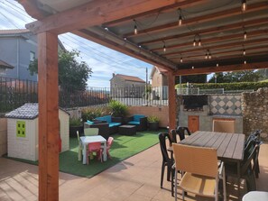 A covered patio area with a wooden pergola, outdoor seating, a barbecue grill, and a small playhouse.