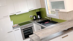 A modern kitchen with white cabinets, a green backsplash, a built-in oven, a coffee maker, and a window above the sink.