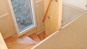 A wooden staircase leading to a room with a window, a door with a handle, and a carpeted floor.