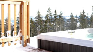 A hot tub with a wooden deck and a snowy landscape in the background.