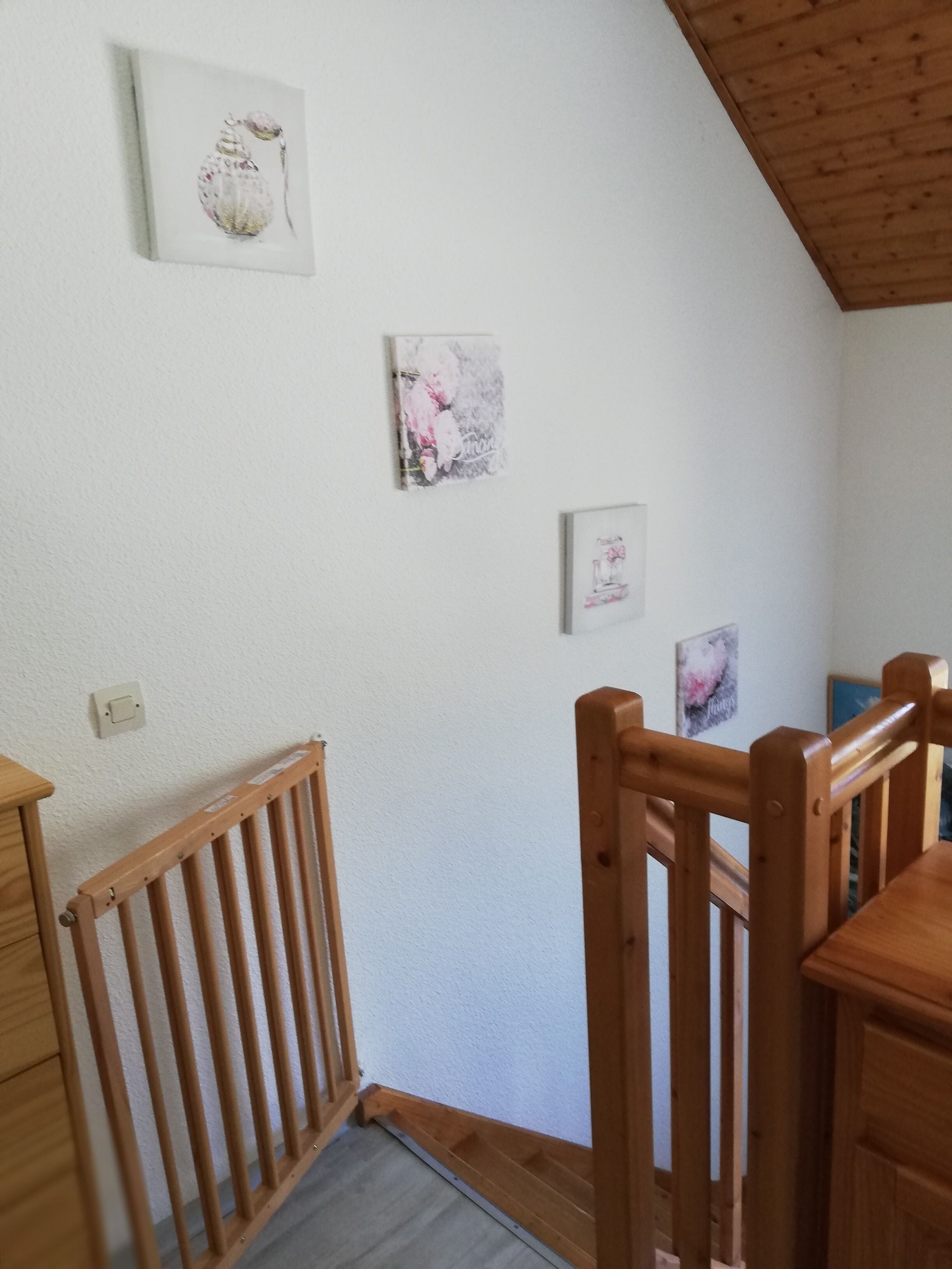 Una stanza con una sedia di legno, un piccolo tavolo e una ringhiera in legno. Sulla parete ci sono tre quadri incorniciati.