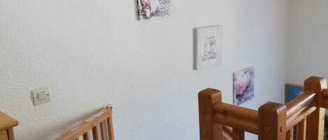 Una stanza con una sedia di legno, un piccolo tavolo e una ringhiera in legno. Sulla parete ci sono tre quadri incorniciati.