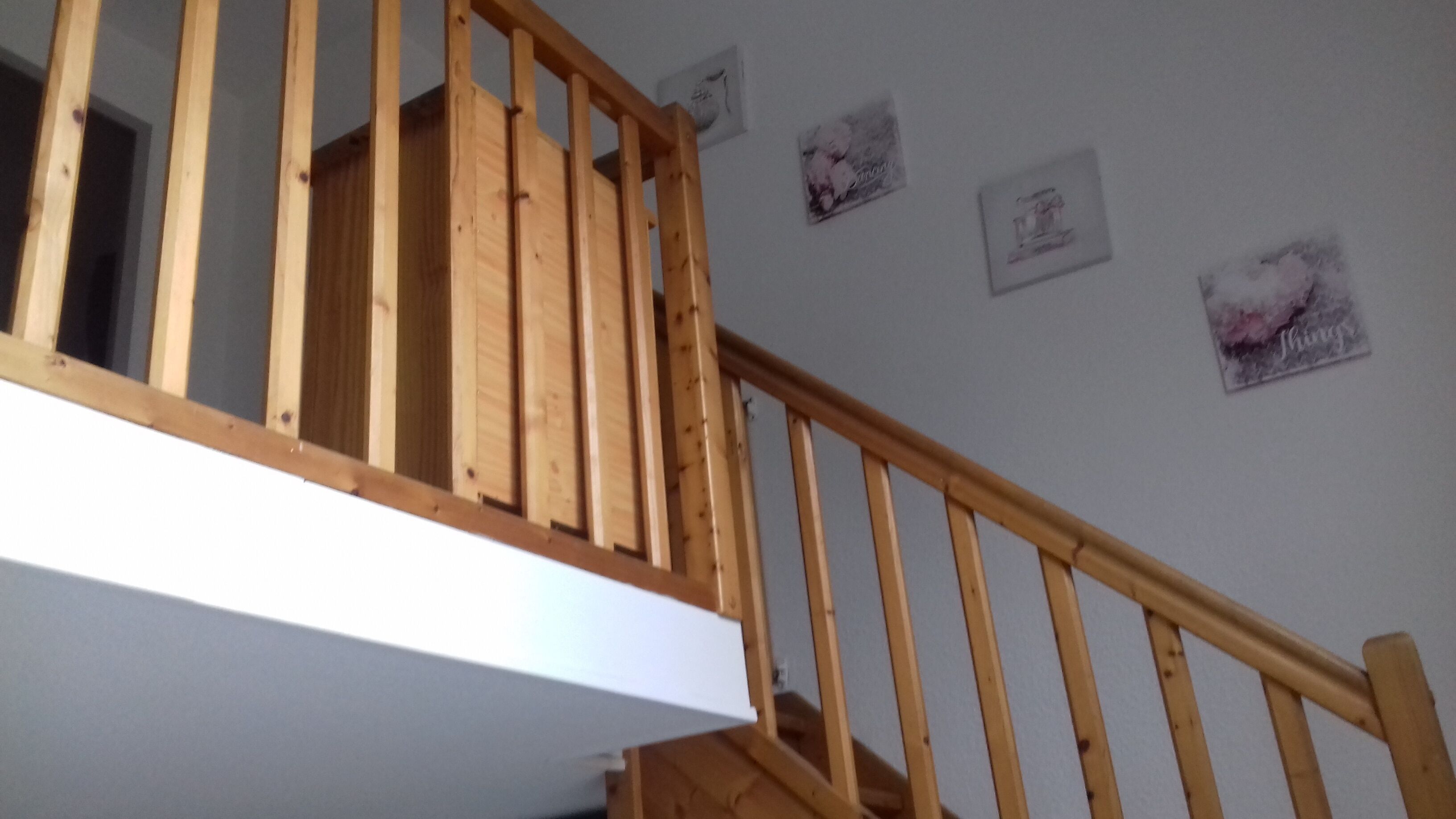 Un escalier en bois avec une rampe, des murs blancs et de petits tableaux encadrés.