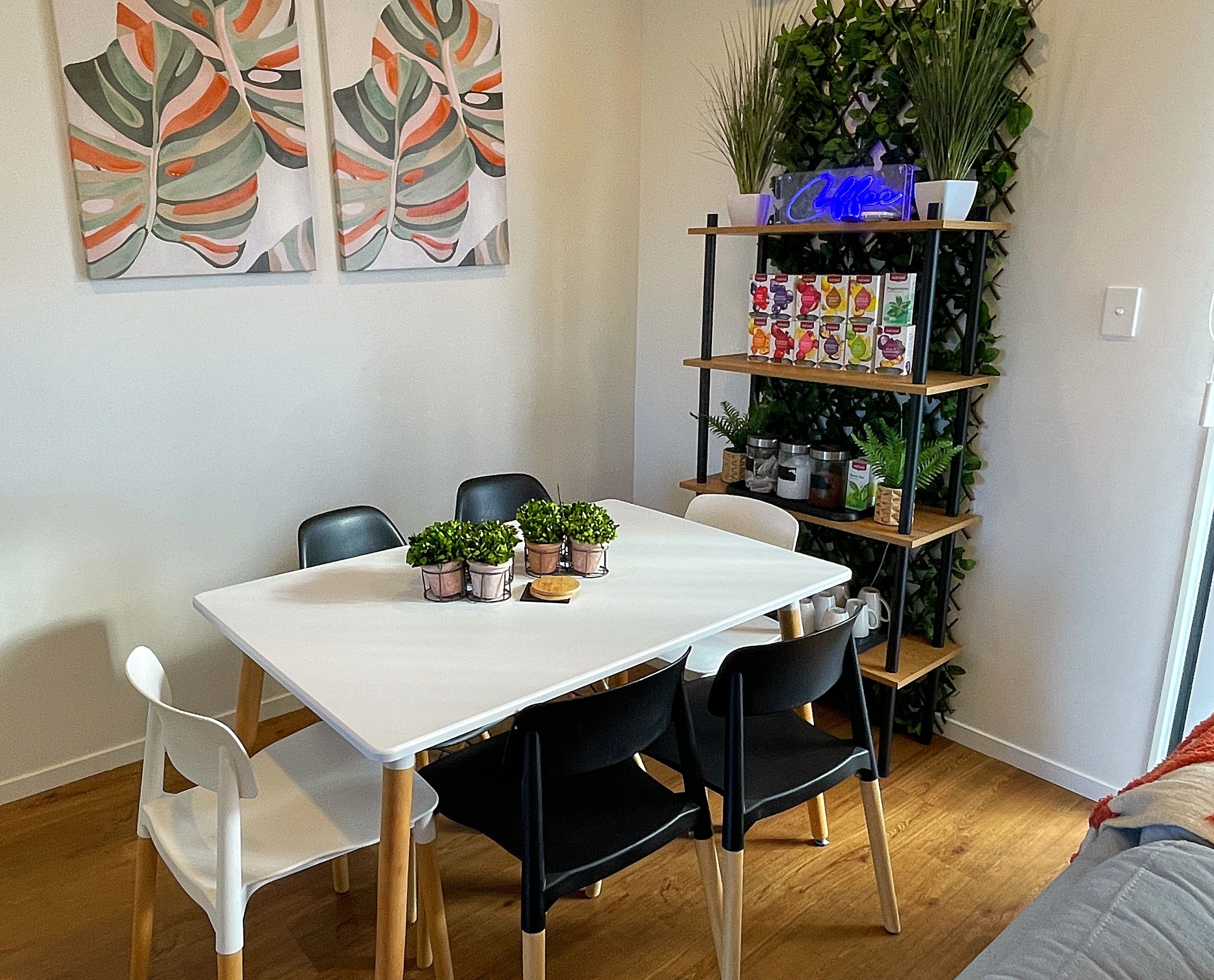 A dining area with a white table, black chairs, and a potted plant arrangement.