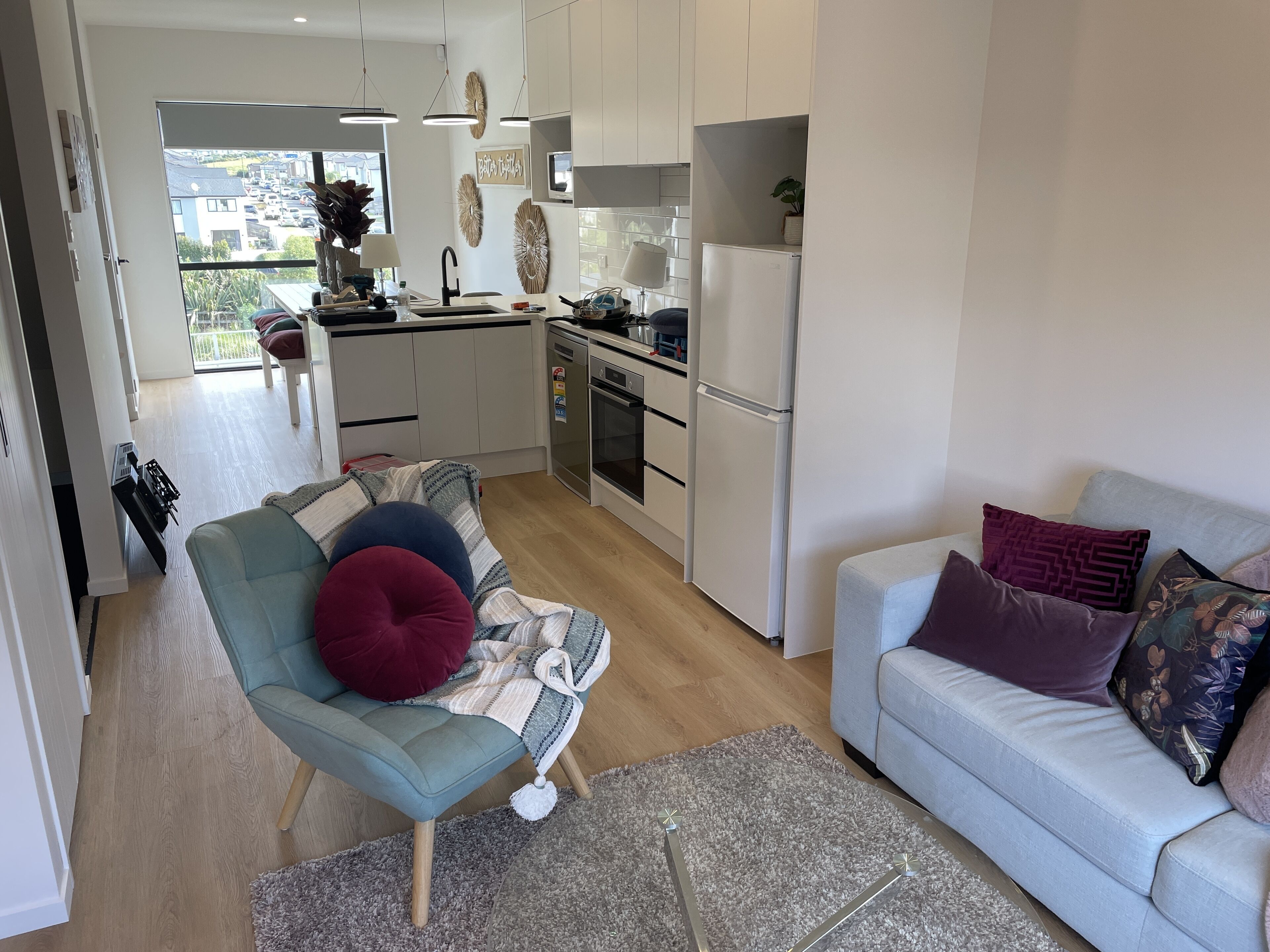 A modern kitchen with white cabinets, a built-in oven, and a refrigerator. There is a dining area with a table and chairs, and a living room with a sofa and a coffee table.