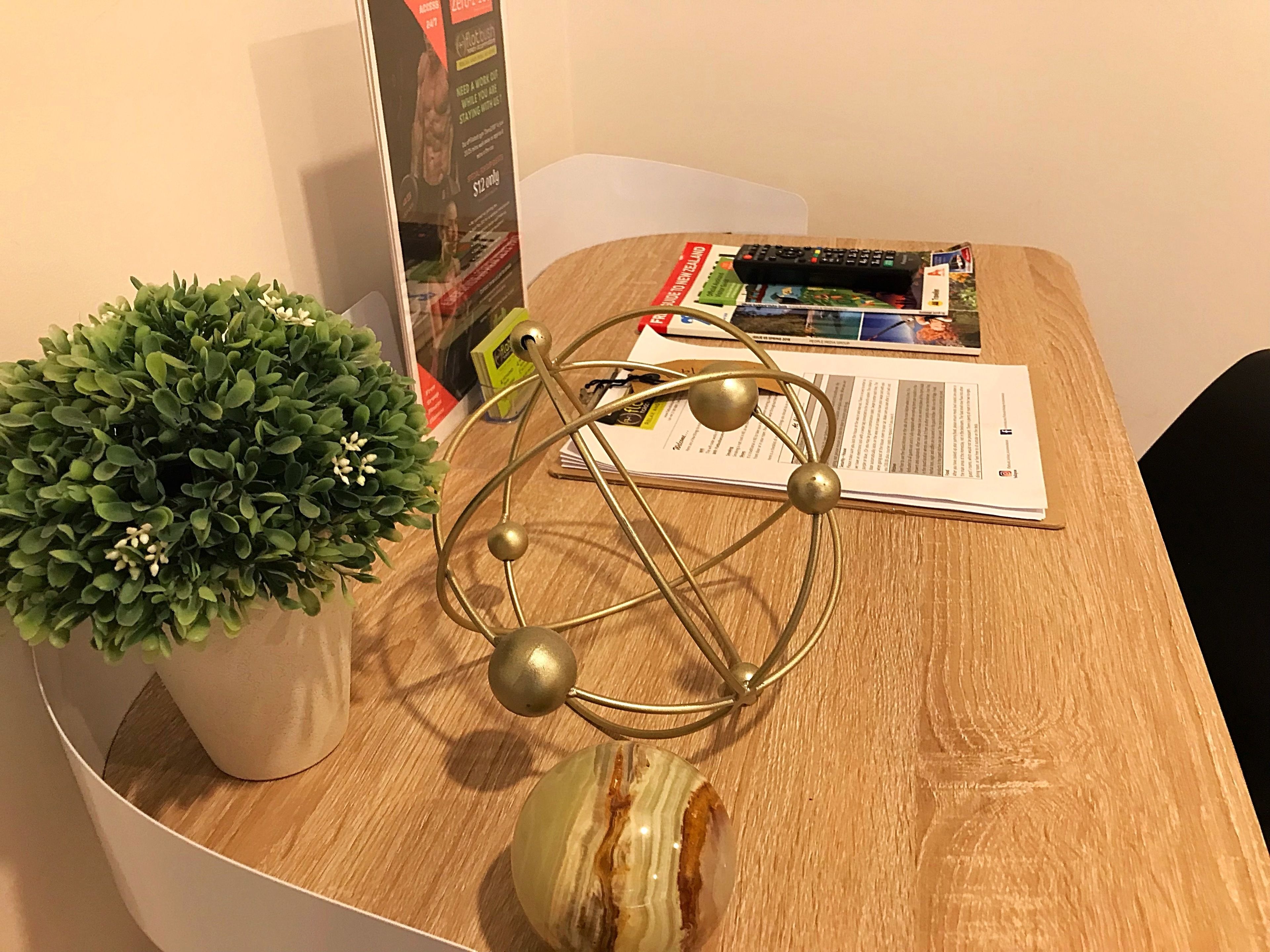 Una mesa de madera con una planta en maceta, una esfera metálica decorativa y algunos papeles.